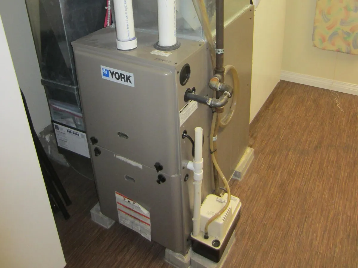 Condensing gas furnace in a utility room with white PVC vent pipes, gas line and condensate pump